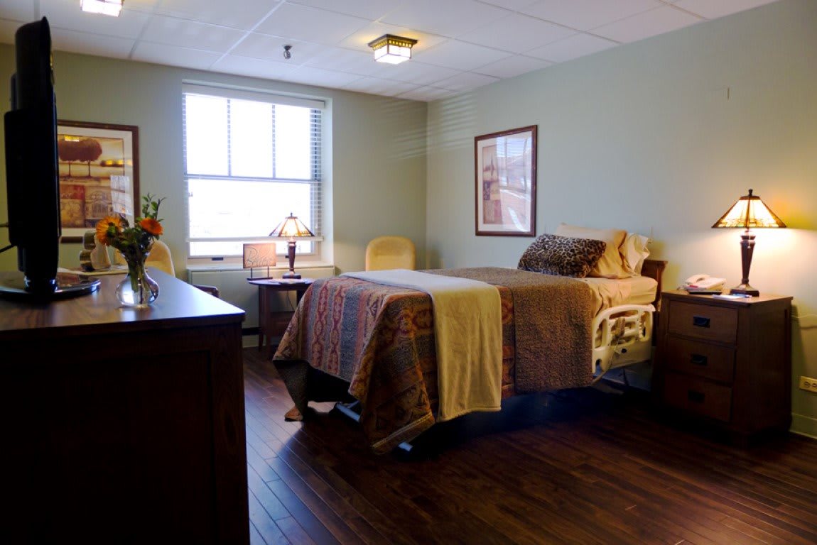 A cozy hospital room with a single bed, window, and wooden flooring.