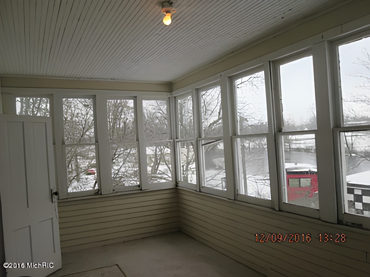An enclosed porch with large windows showing a snowy winter scene outside.
