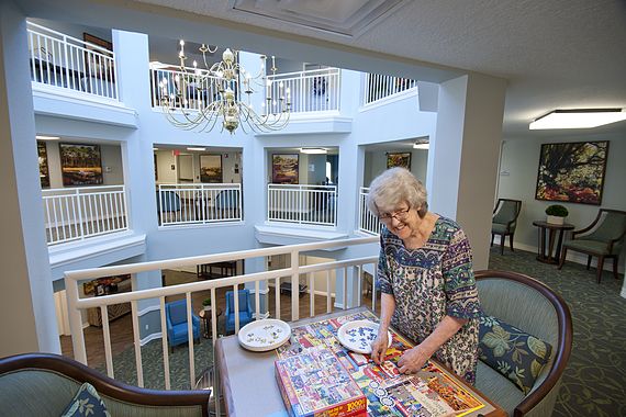 An elderly woman enjoying a puzzle in a bright and spacious lobby area.
