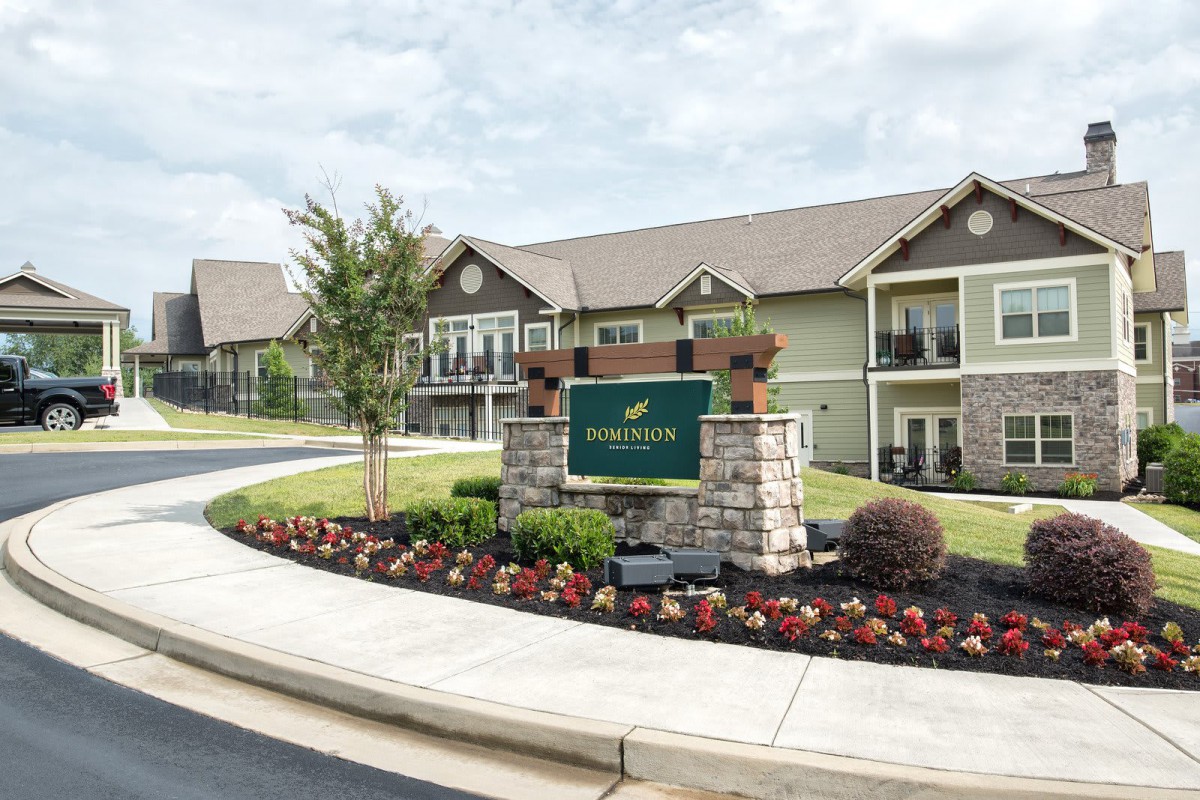 Entrance to an apartment complex with well-maintained landscaping and a welcome sign.