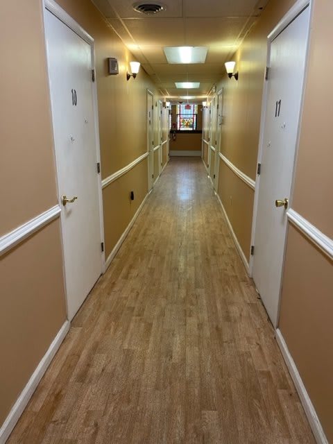 A long, empty hallway with wooden flooring and white doors on either side.