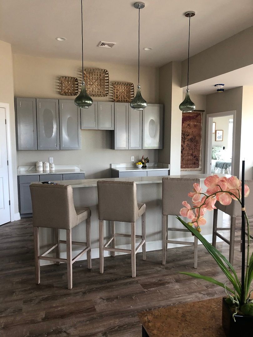 A modern kitchen with gray cabinets and a sleek countertop, accented by pendant lights and bar stools.