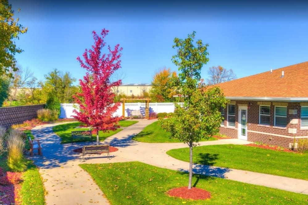 A peaceful park scene with vibrant autumn trees, a winding walkway, and a bench near a small building.