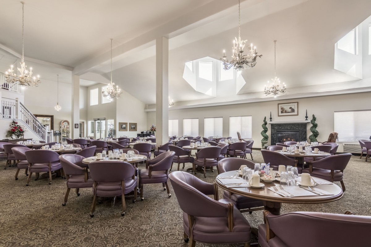 An elegant dining room with chandeliers, set tables, and comfortable seating.