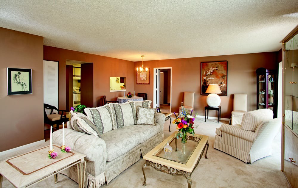 A spacious living room with classic decor, featuring a patterned sofa, floral arrangements, and elegant lighting.