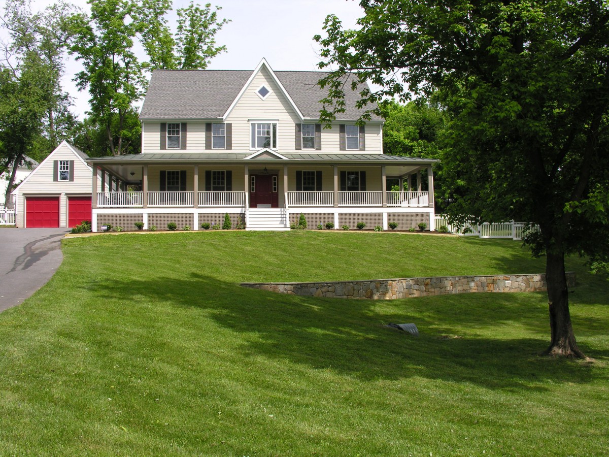 A large house with a spacious porch and a well-maintained lawn, surrounded by trees.
