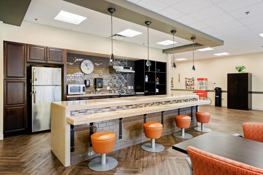 A modern kitchen bar area with orange stools and pendant lighting.