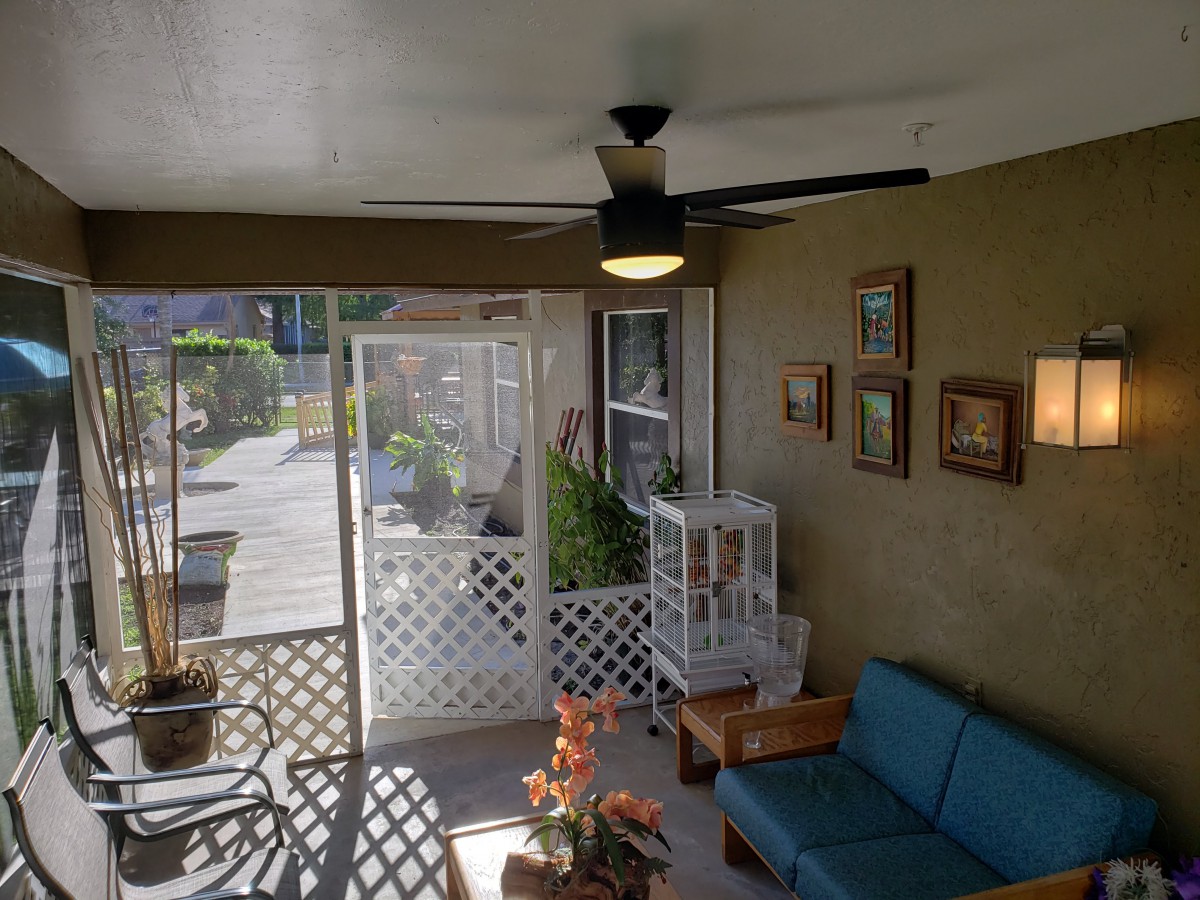 A cozy sunroom with a ceiling fan, couch, and potted plants, featuring large glass doors and wall art.