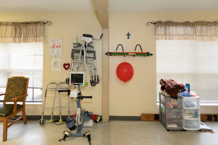 A hospital room corner featuring various medical and safety equipment, including a walker, heart monitor, emergency stretcher, and fire safety tools.