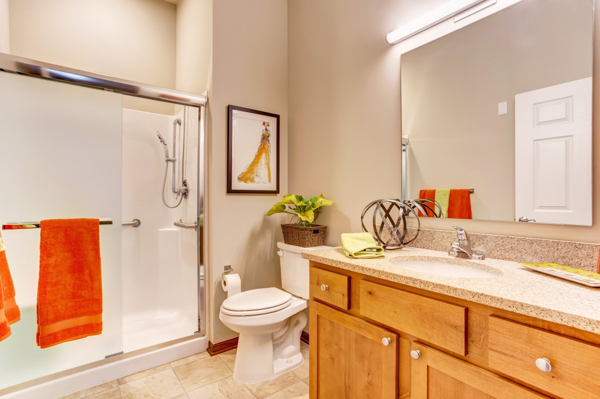 A modern bathroom featuring a glass shower, wooden cabinets, and bright lighting.