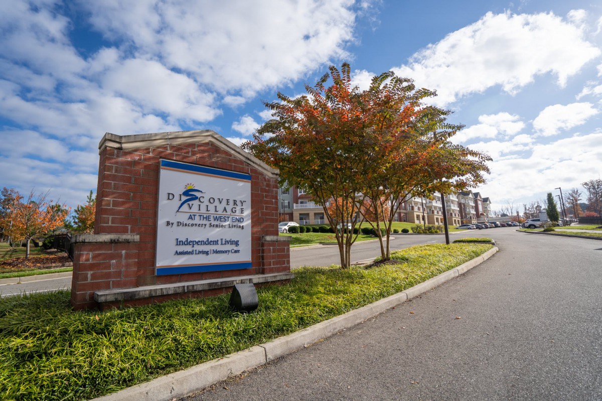 Entrance sign of an apartment complex with landscaped greenery and a cloudy sky.