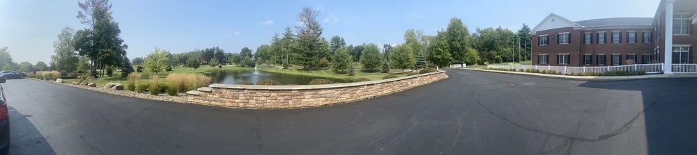 A scenic landscape featuring a stone wall alongside a road, with trees and a pond in the background.