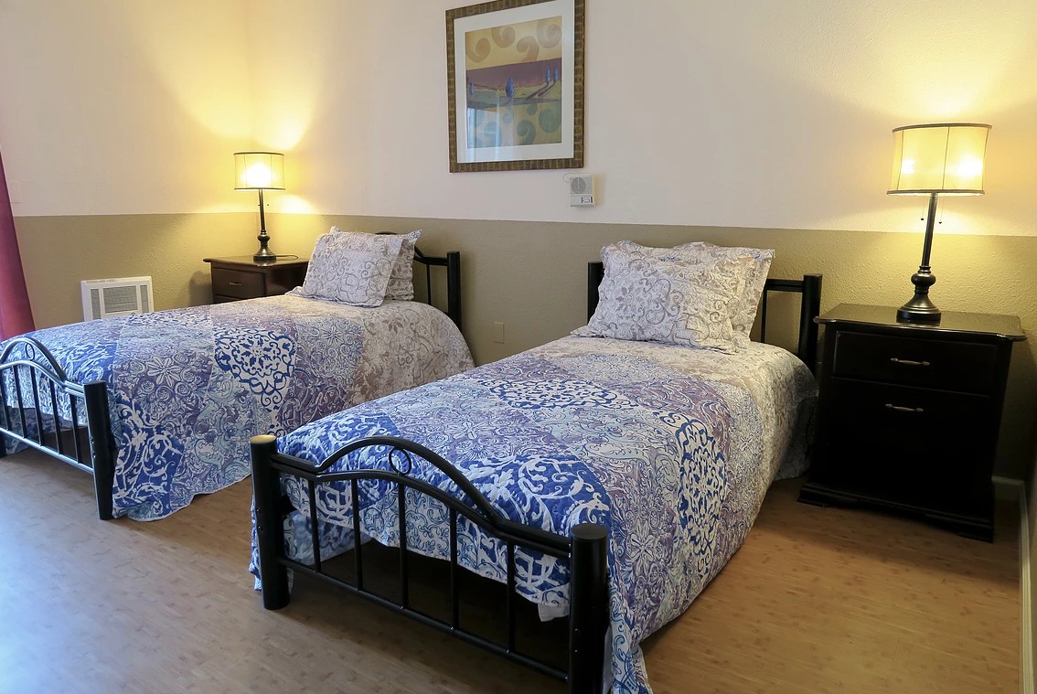 A cozy bedroom with two twin beds adorned with patterned bedding and lit by a bedside lamp.