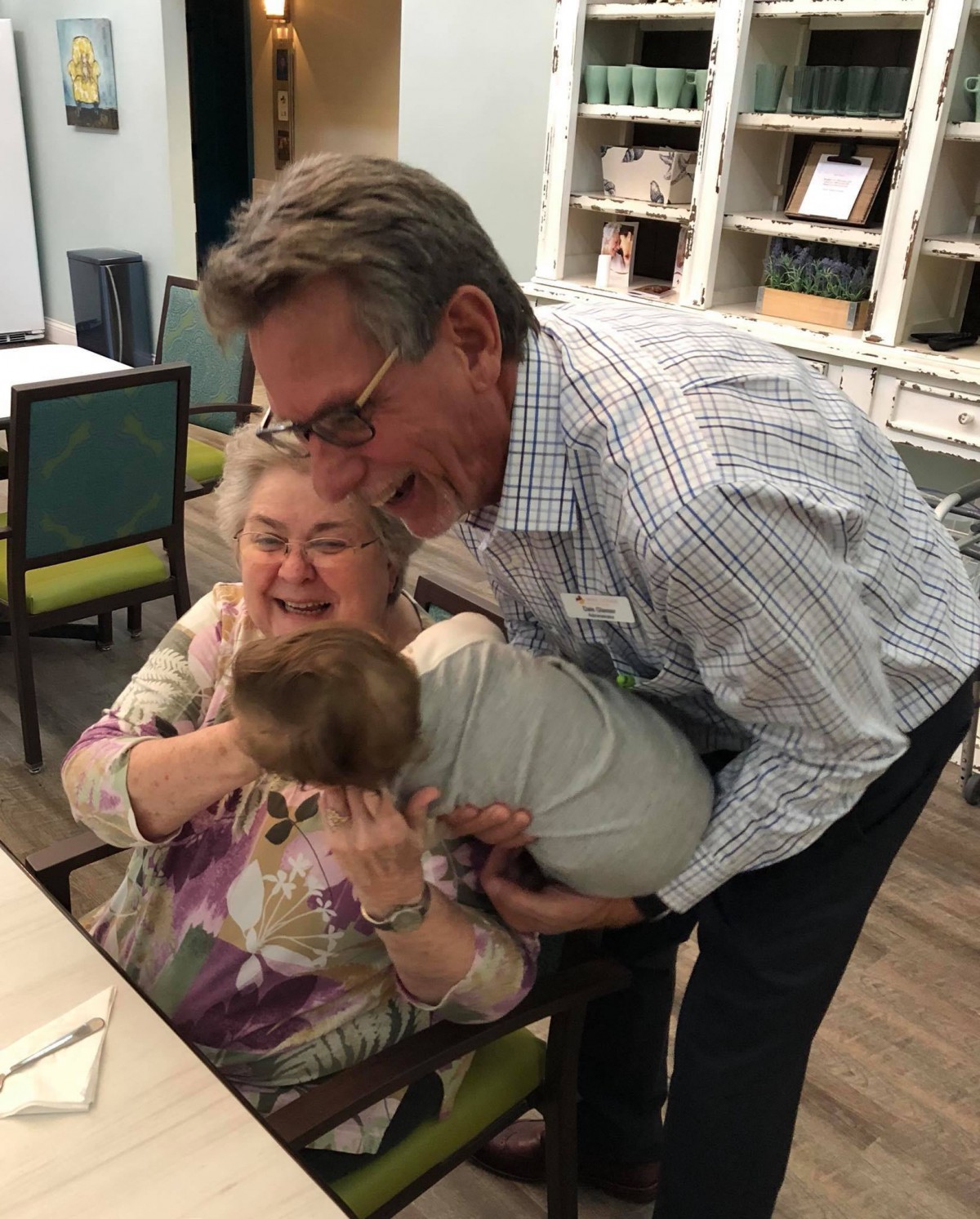 A joyful family moment with an elderly couple and a baby sharing a warm hug.