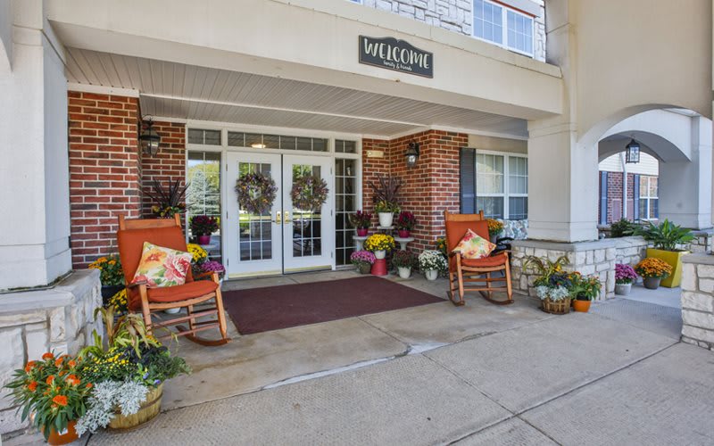 The entrance to a building is decorated with rocking chairs and flower pots, creating a welcoming atmosphere.