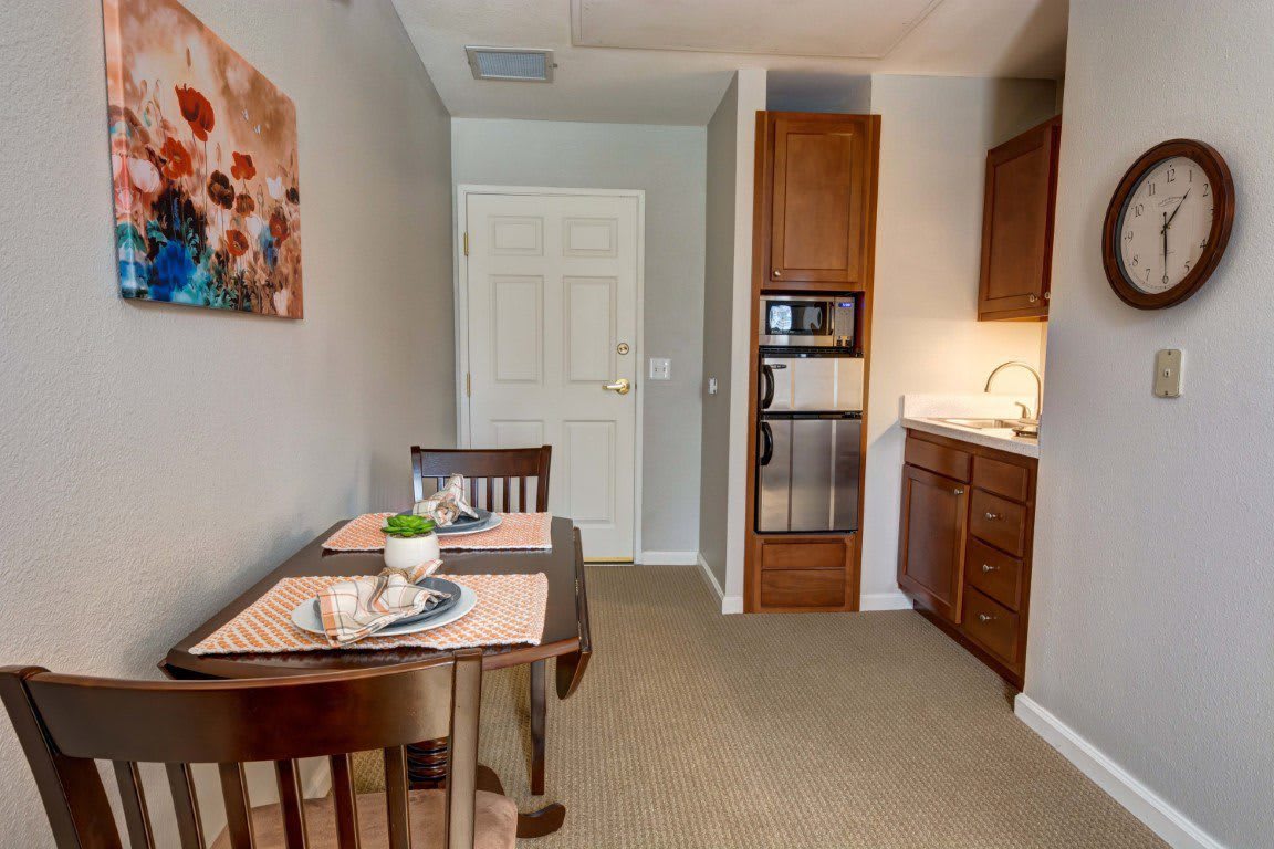 A cozy kitchenette and dining area featuring a small table set for two, wooden cabinets, a microwave, and a sink.