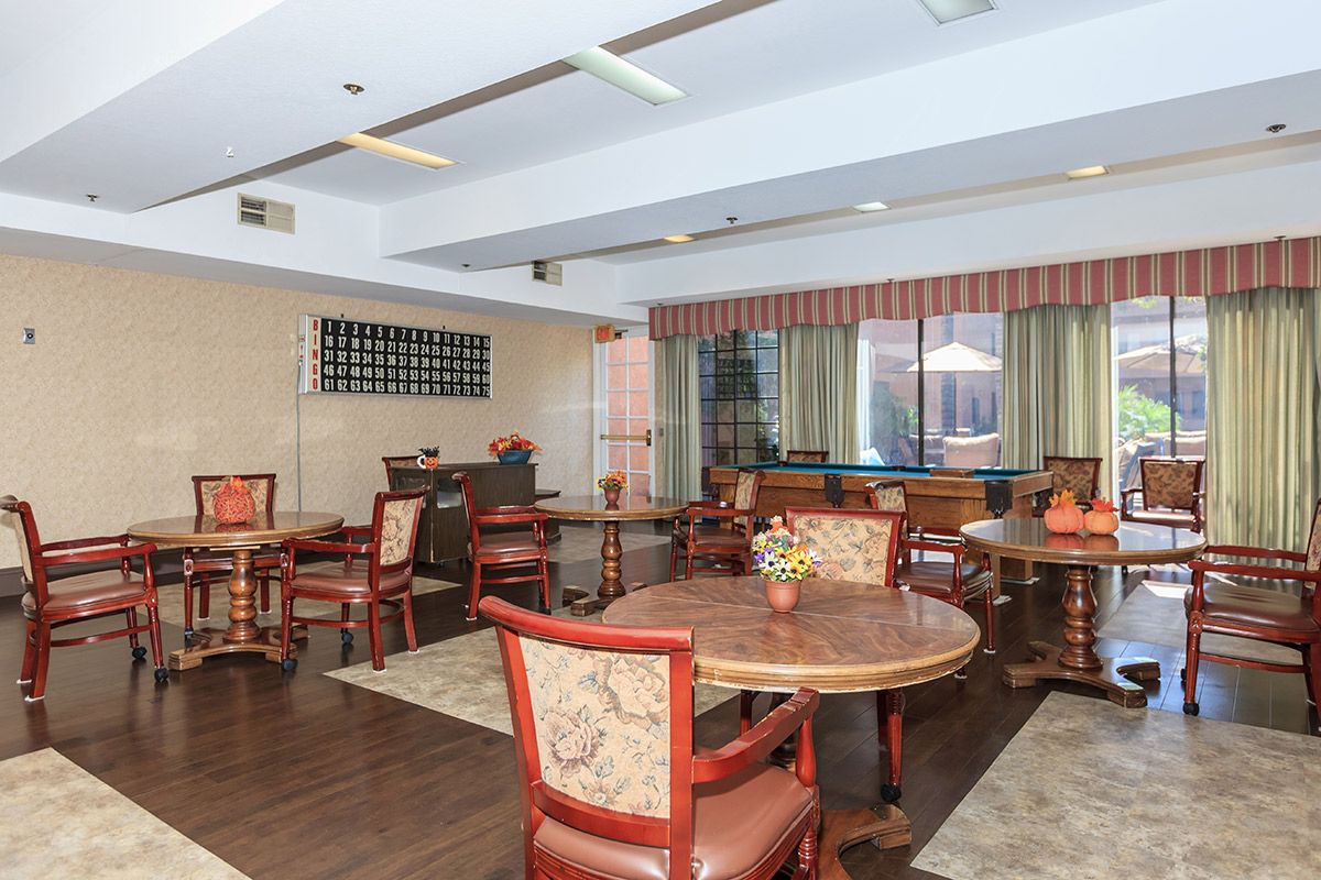 A cozy dining area with round tables and wooden chairs, accented by large windows and curtains.