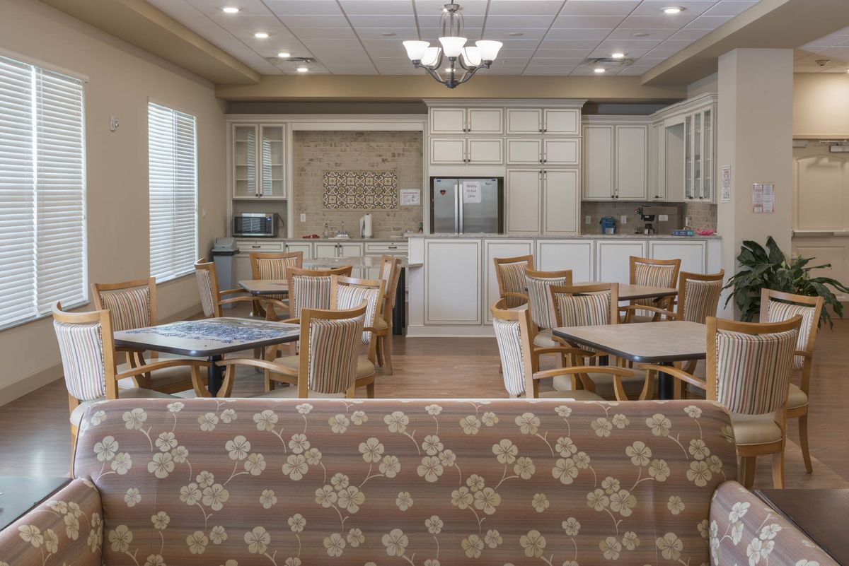 A spacious kitchen and dining area with multiple tables and chairs, featuring elegant lighting and cabinetry.