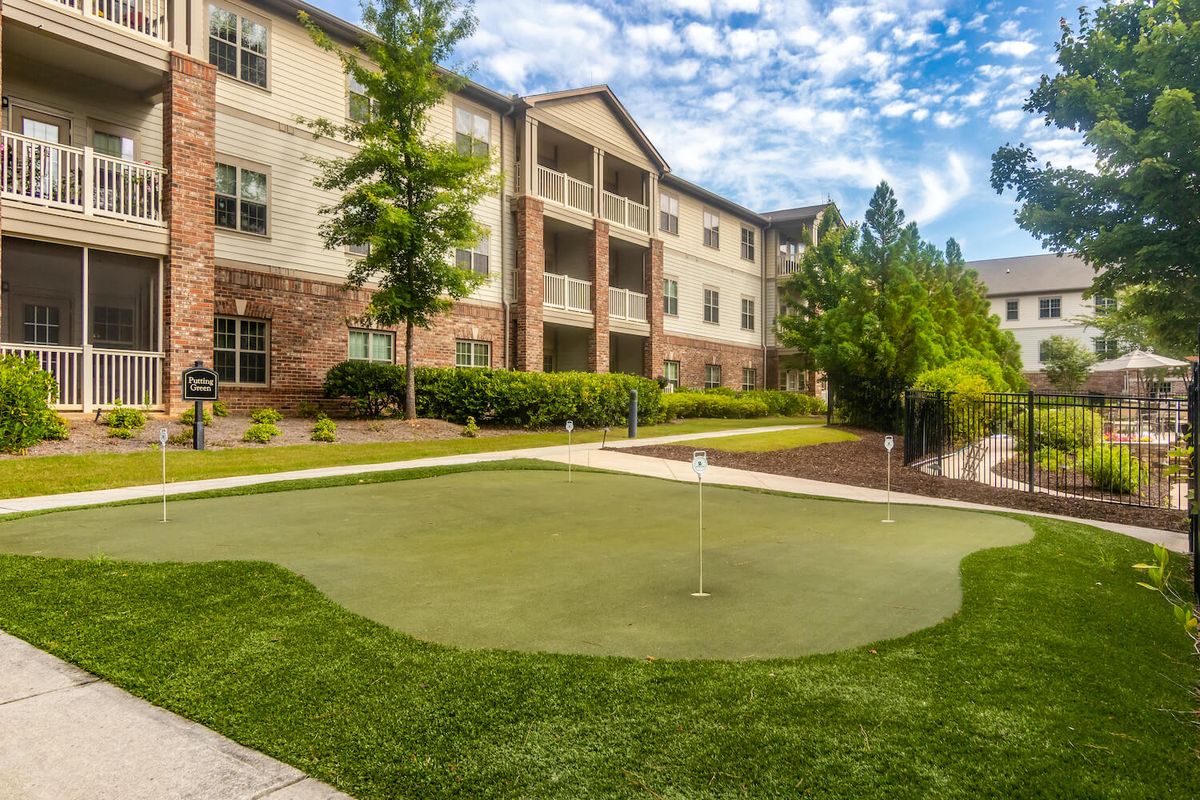 An outdoor view of an apartment complex with a well-maintained putting green and landscaped gardens.