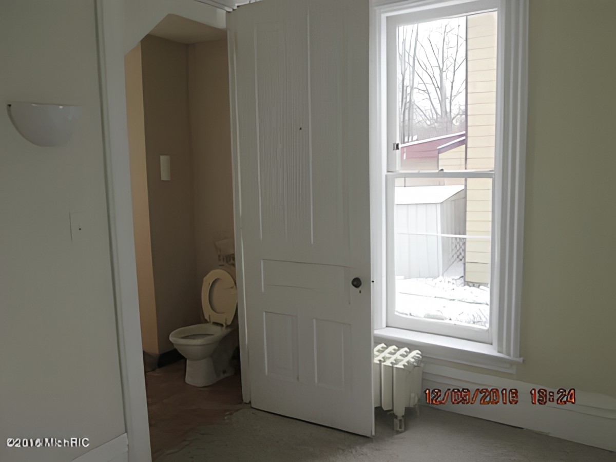 A room with a partially open door revealing a toilet, next to a large window with an outside view.