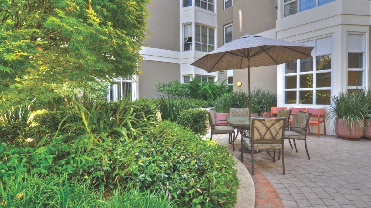 A serene patio area with outdoor seating and lush greenery, set against the backdrop of an apartment building.
