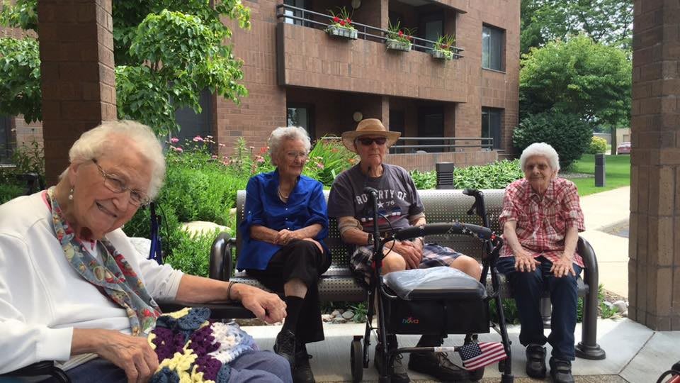 A group of seniors sitting and conversing in an outdoor garden setting.