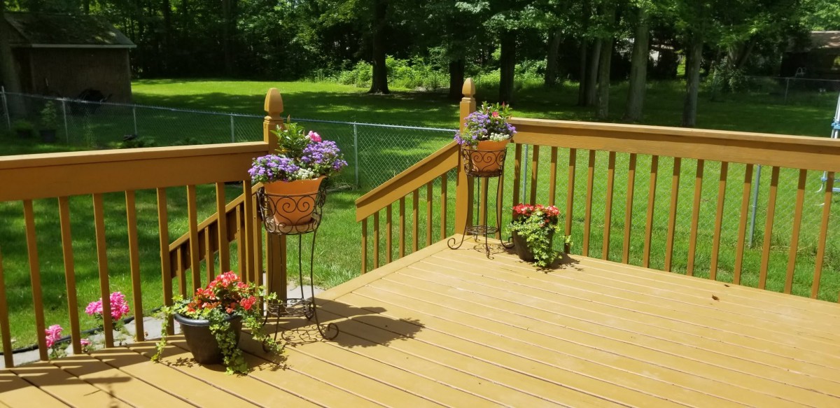 A sunny wooden deck adorned with colorful flowers in planters overlooking a lush garden.