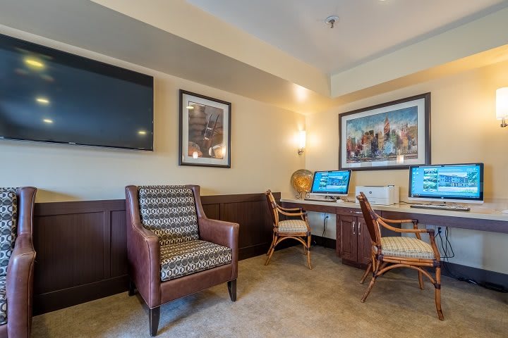 A cozy office workspace featuring a desk with computers, comfortable seating, and decorative artwork on the walls.