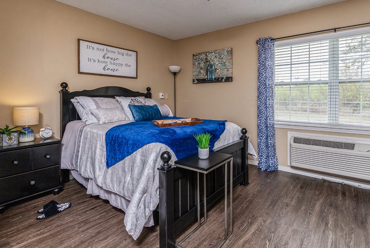 A cozy bedroom interior with a neatly made bed, blue accents, and wooden flooring.