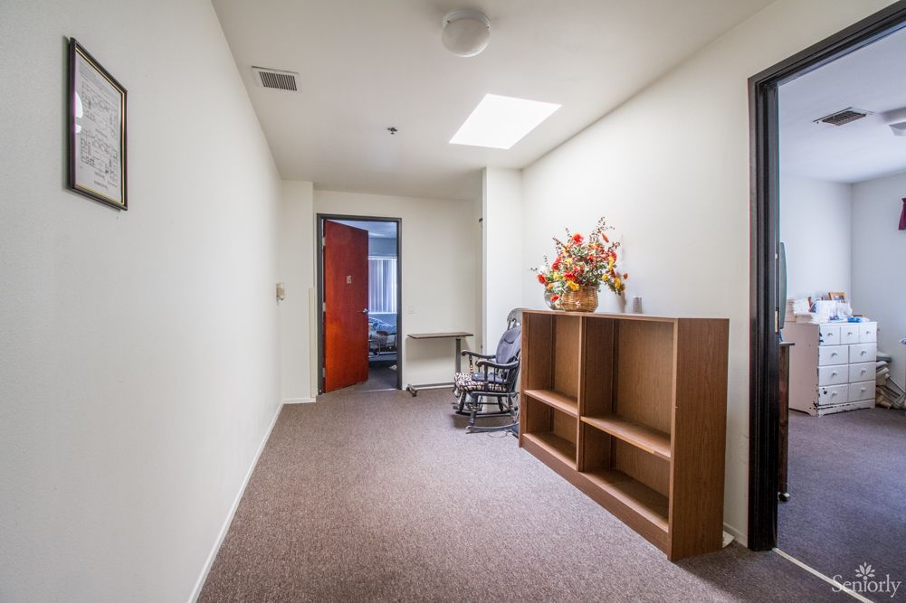 A simple hallway with a rocking chair, bookshelf, and floral arrangement.