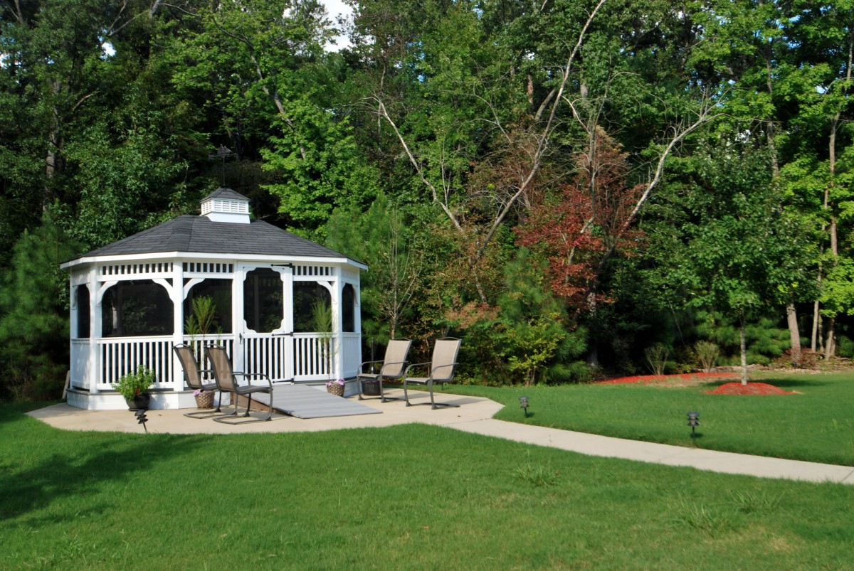 A scenic outdoor setting with a white gazebo, surrounded by lush greenery and chairs on a well-maintained lawn.
