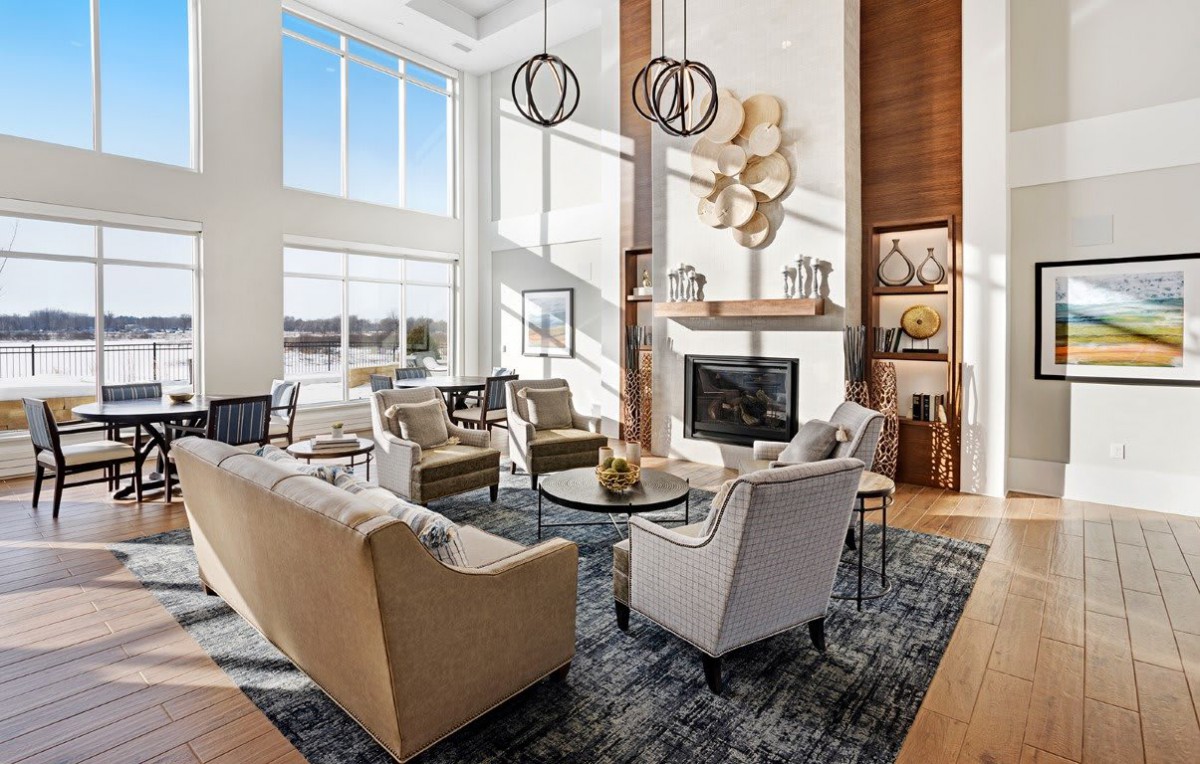 A modern living room with high ceilings, large windows, and contemporary furniture centered around a fireplace.
