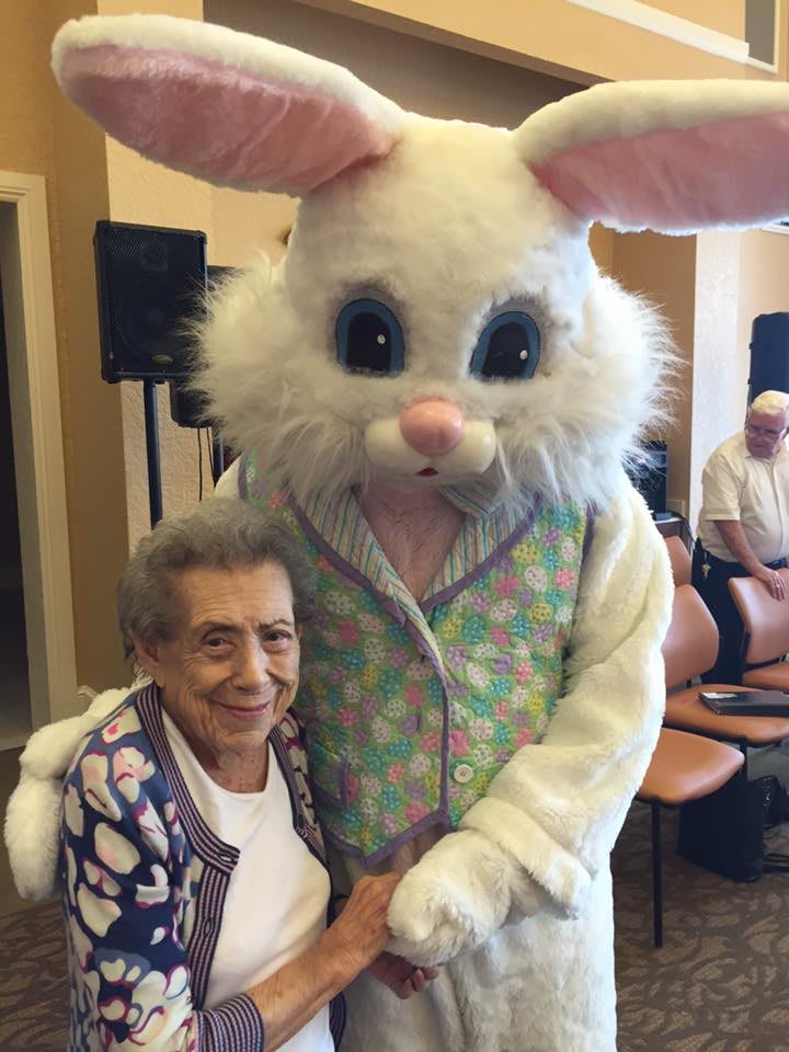 An elderly woman smiling alongside a person in an Easter Bunny costume during a celebration.