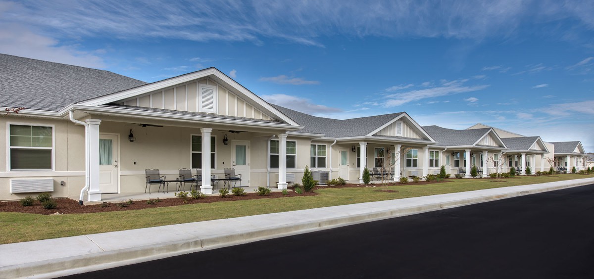 A row of single-story suburban houses with front porches under a clear blue sky.