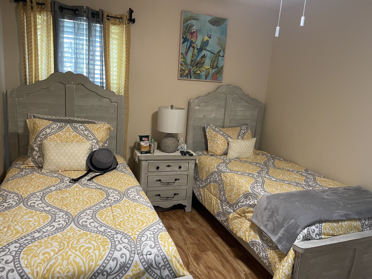 A cozy bedroom with two twin beds featuring matching yellow bedding, a central nightstand, and vibrant artwork on the wall.