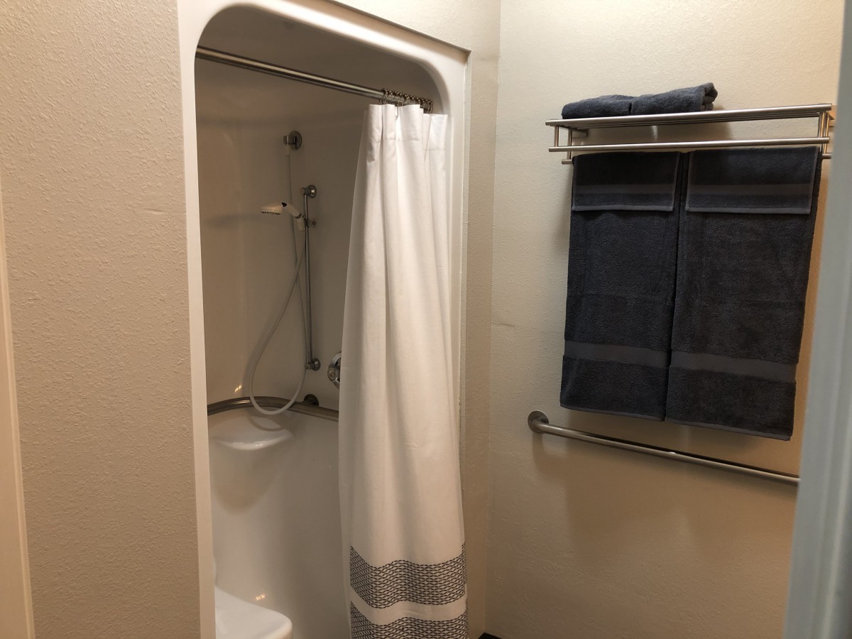 A clean bathroom featuring a shower with a white curtain and neatly folded towels on a rack.