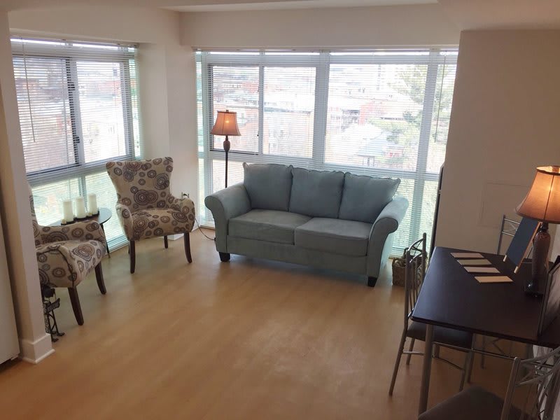 A bright living room with a sofa, chairs, and large windows letting in natural light.
