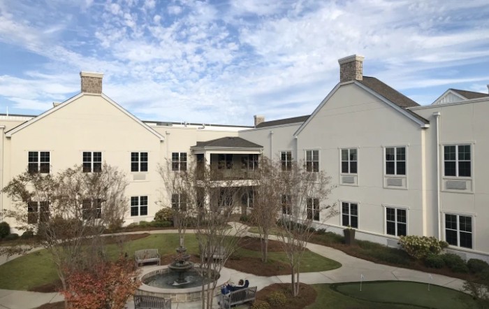 A view of a modern building with a courtyard and landscaped surroundings under a partly cloudy sky.