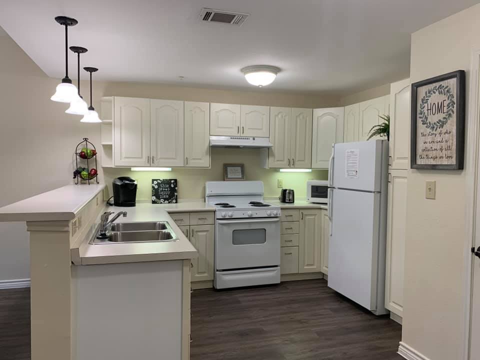 A modern kitchen featuring white cabinets, a refrigerator, stove, and sink with stylish pendant lighting.