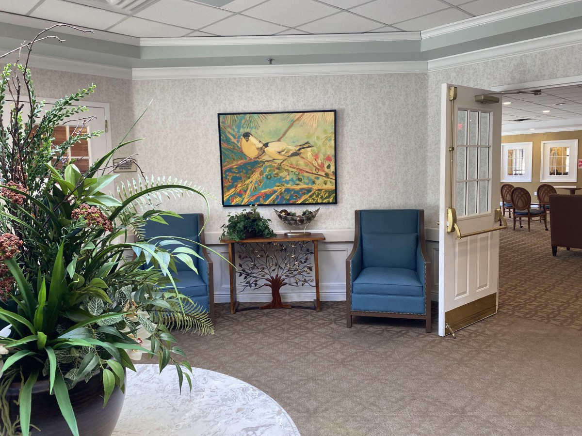 A cozy waiting room with blue chairs, a decorative table, and a painting on the wall.