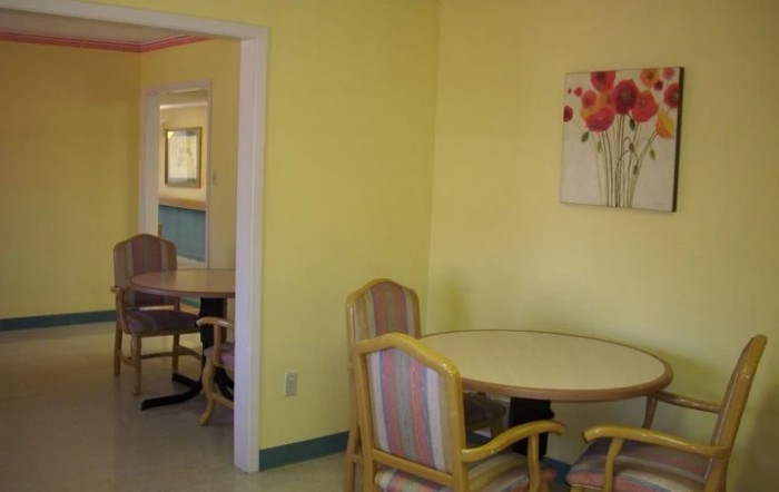 A cozy room with yellow walls, featuring a round table and chairs, adorned with artwork.