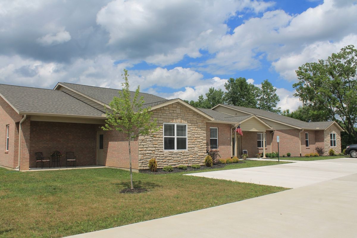 A suburban residential house with a driveway and small trees under a partly cloudy sky.