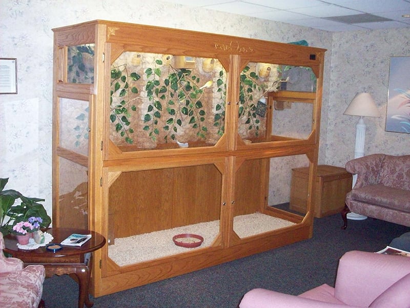 A large wooden enclosure in a living room setting, featuring multiple compartments and decorative plants.