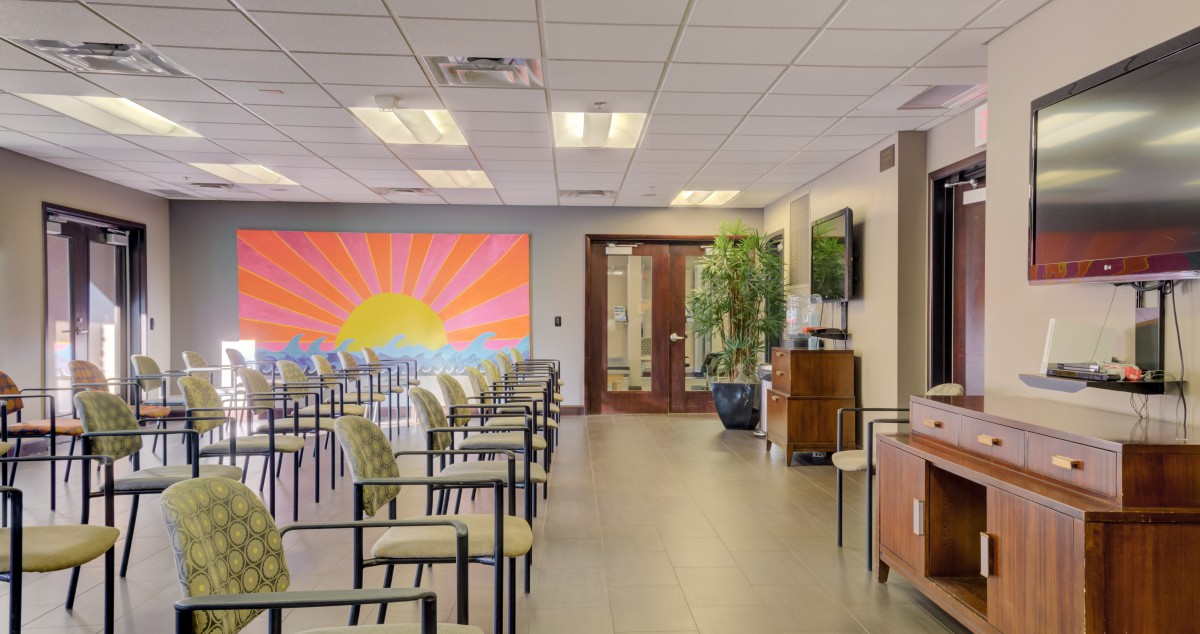 A spacious waiting room with rows of chairs and a vibrant sunset mural on the wall.