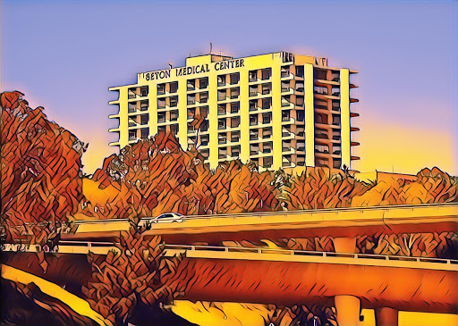 A vibrant view of a medical center building framed by trees and a highway, set against a colorful sunset sky.