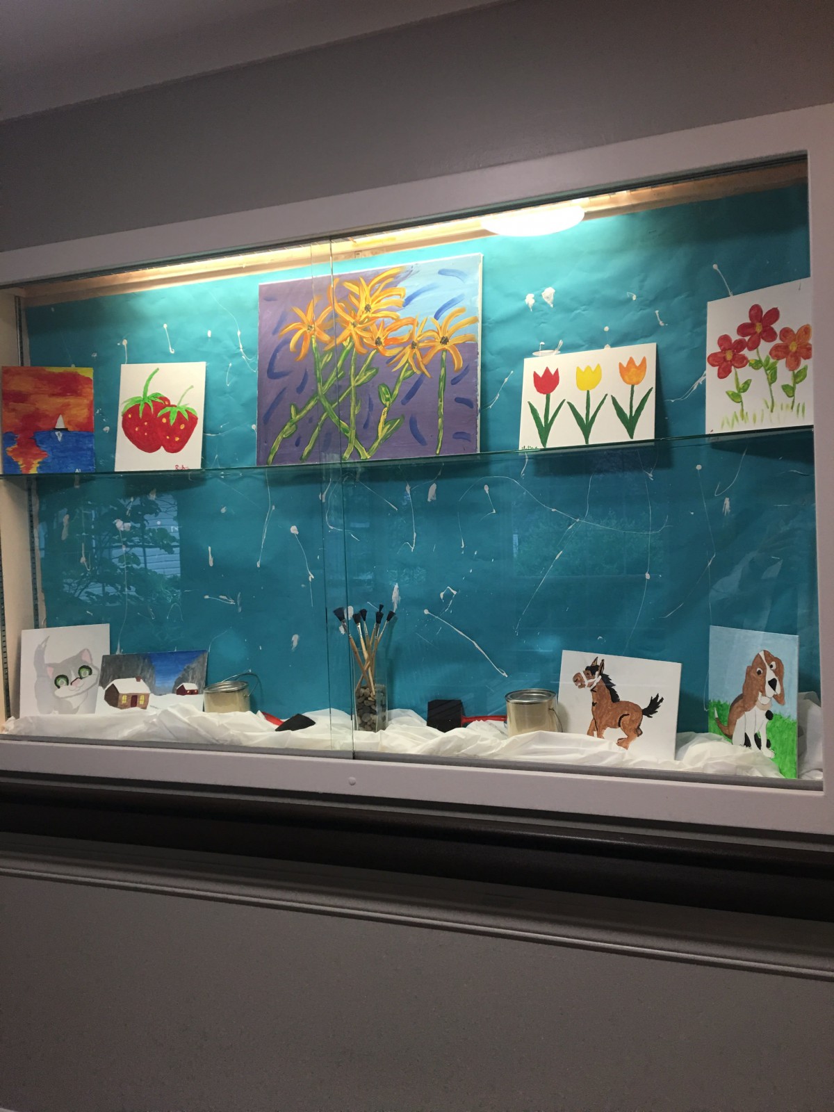 A display case featuring colorful paintings and drawings of flowers and animals.