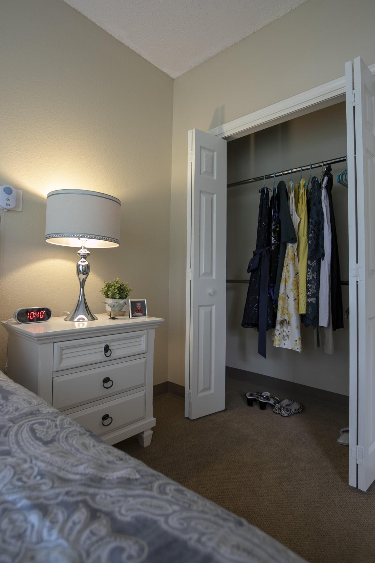 A cozy bedroom with a nightstand and an open closet displaying hanging clothes.