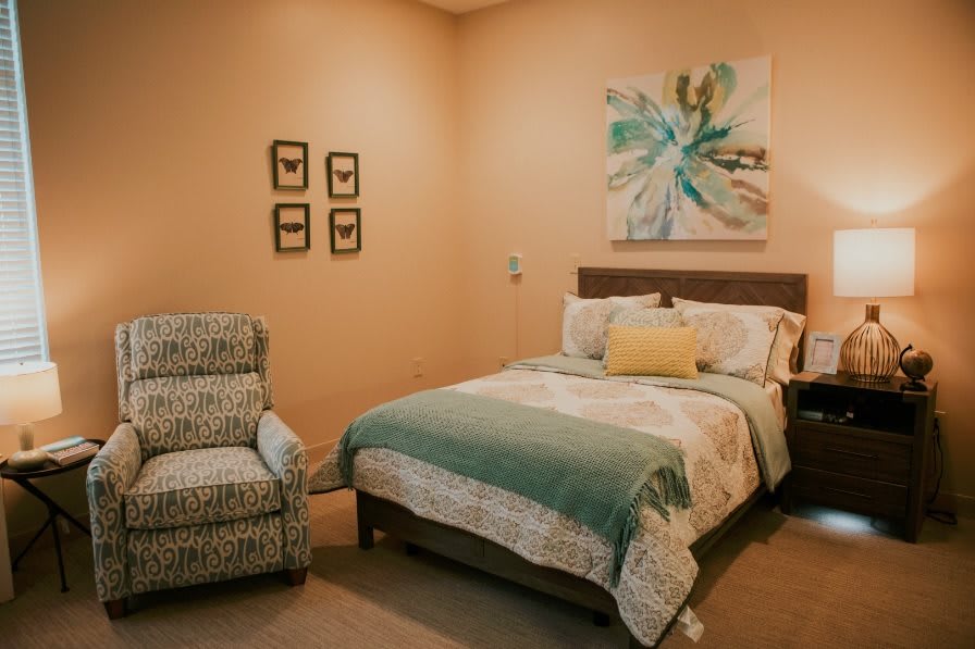 A cozy bedroom with a neatly made bed and an armchair, complemented by wall art.