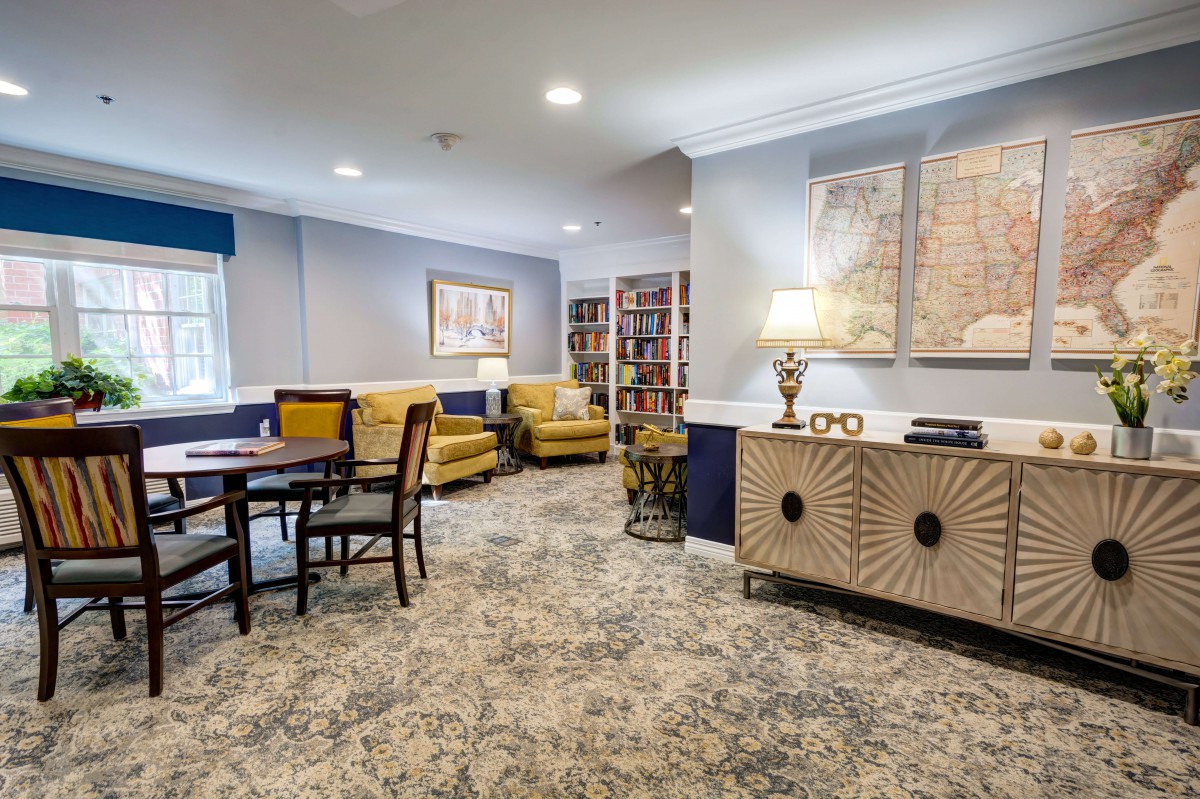 A cozy living room with stylish furniture, including yellow chairs, a carpeted floor, a bookshelf, and decorative artwork.