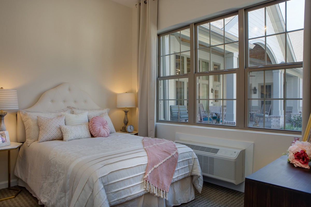 A cozy, modern bedroom with a neatly made bed, decorative pillows, and large windows allowing natural light to fill the room.